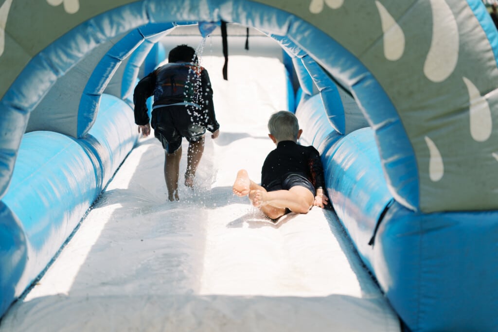 1 child running and 1 child sliding down a water slide, side by side